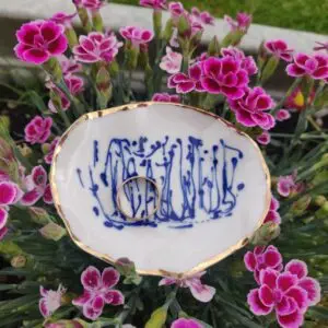 A Blue and White Porcelain Ring Holder with gold lustre is surrounded by vibrant pink flowers, showcasing its small white dish adorned with intricate blue patterns.