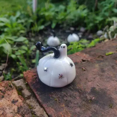 Ghostly Porcelain Pumpkins with black accents on a brick surface, surrounded by greenery.