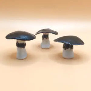 Three ceramic mushrooms with dark caps and light stems are arranged on a beige surface.