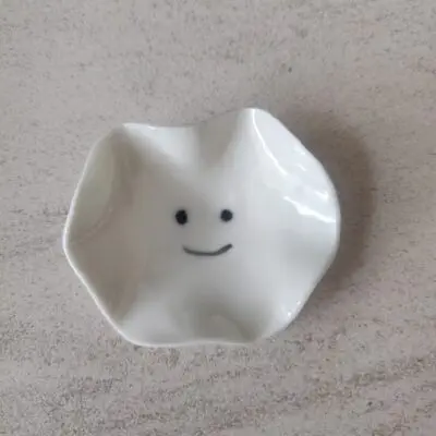 A compact, white ceramic dish featuring a wavy edge and adorned with a minimalist smiley face design at its base, known as the Mini Smiley Face.