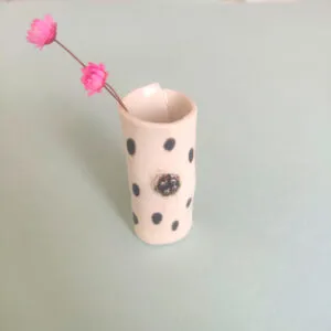 Speckled Mini Pottery Vase, featuring a black polka dot design, holding two small pink flowers, set against a light green background.